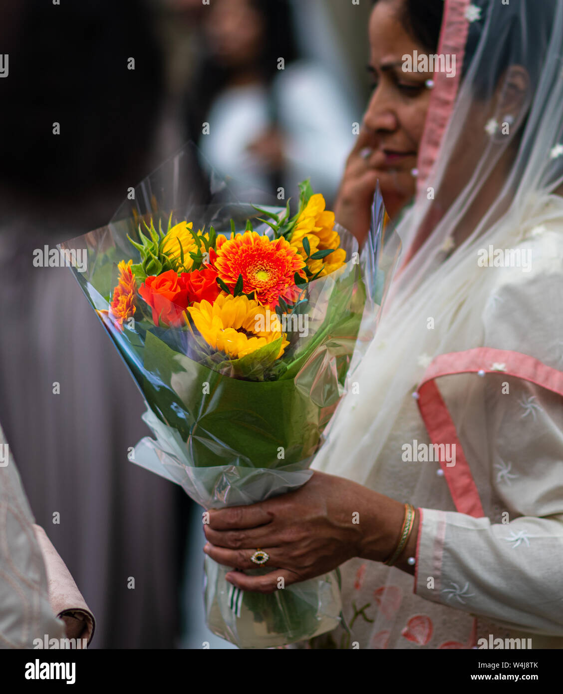 SHEFFIELD, UK - 20. Juli 2019: Die Mutter der Braut hält einige schöne helle orange und gelbe Blumen in der Hand nach einer Hochzeit Stockfoto