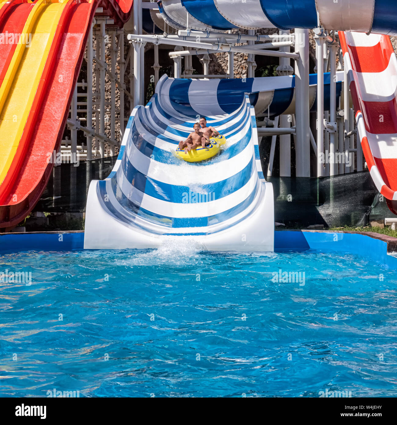 Glücklich lachend Vater und Sohn im Vergnügungspark. Erwachsener und Jugendlicher junge genießen Wochenende zusammen, Reitschule, die Wasserrutsche in Gelb inflatabl Stockfoto