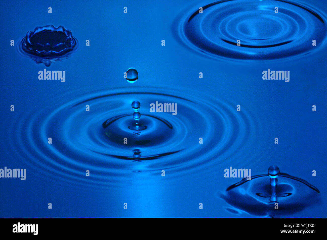 Vier Wassertropfen schaffen verschiedene kreisförmigen Wellen auf blauem Wasser. Stockfoto
