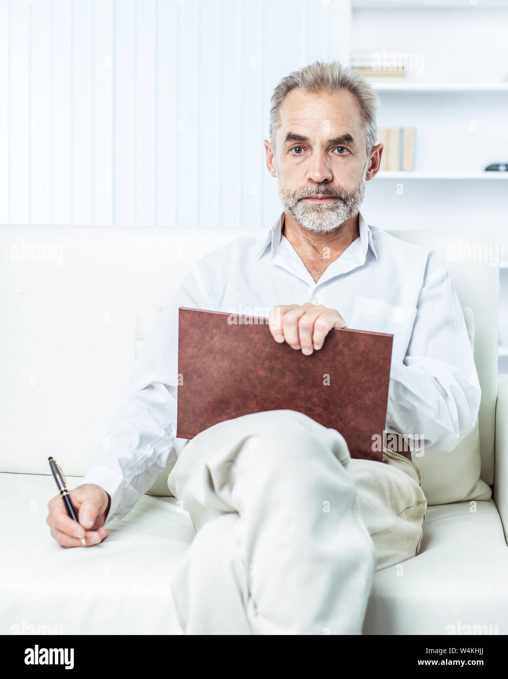 Geschäftsmann mit Stift und Business Magazine, auf einem Stuhl sitzend das moderne Büro Stockfoto