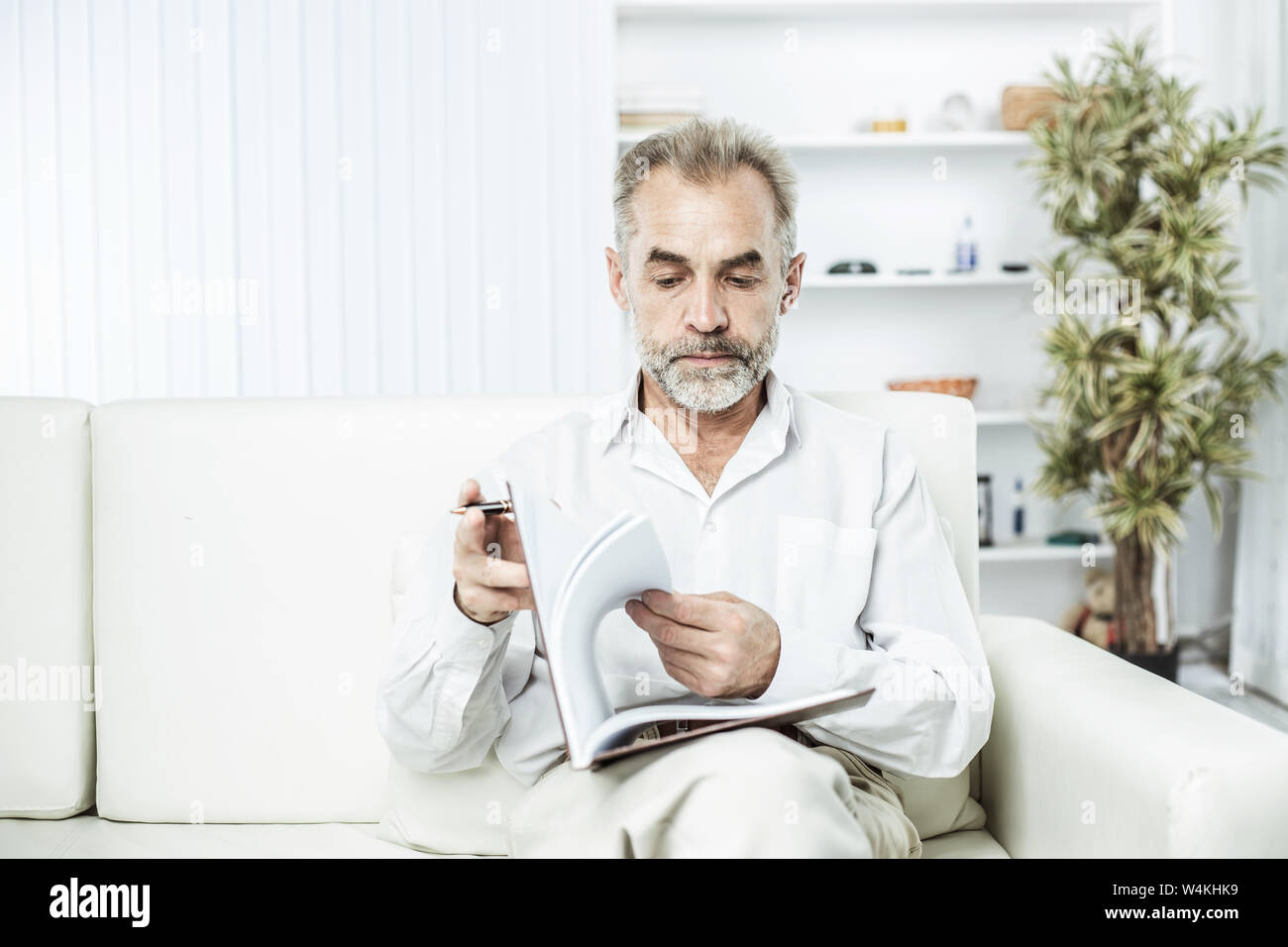 Geschäftsmann mit Stift und Business Magazine, auf einem Stuhl sitzend das moderne Büro Stockfoto