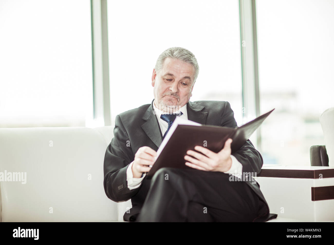 Erfahrenen Rechtsanwalt die Dokumente Bewertungen mit den Bedingungen einer neuen Vertrag auf dem Sofa sitzen im eigenen Büro. Stockfoto