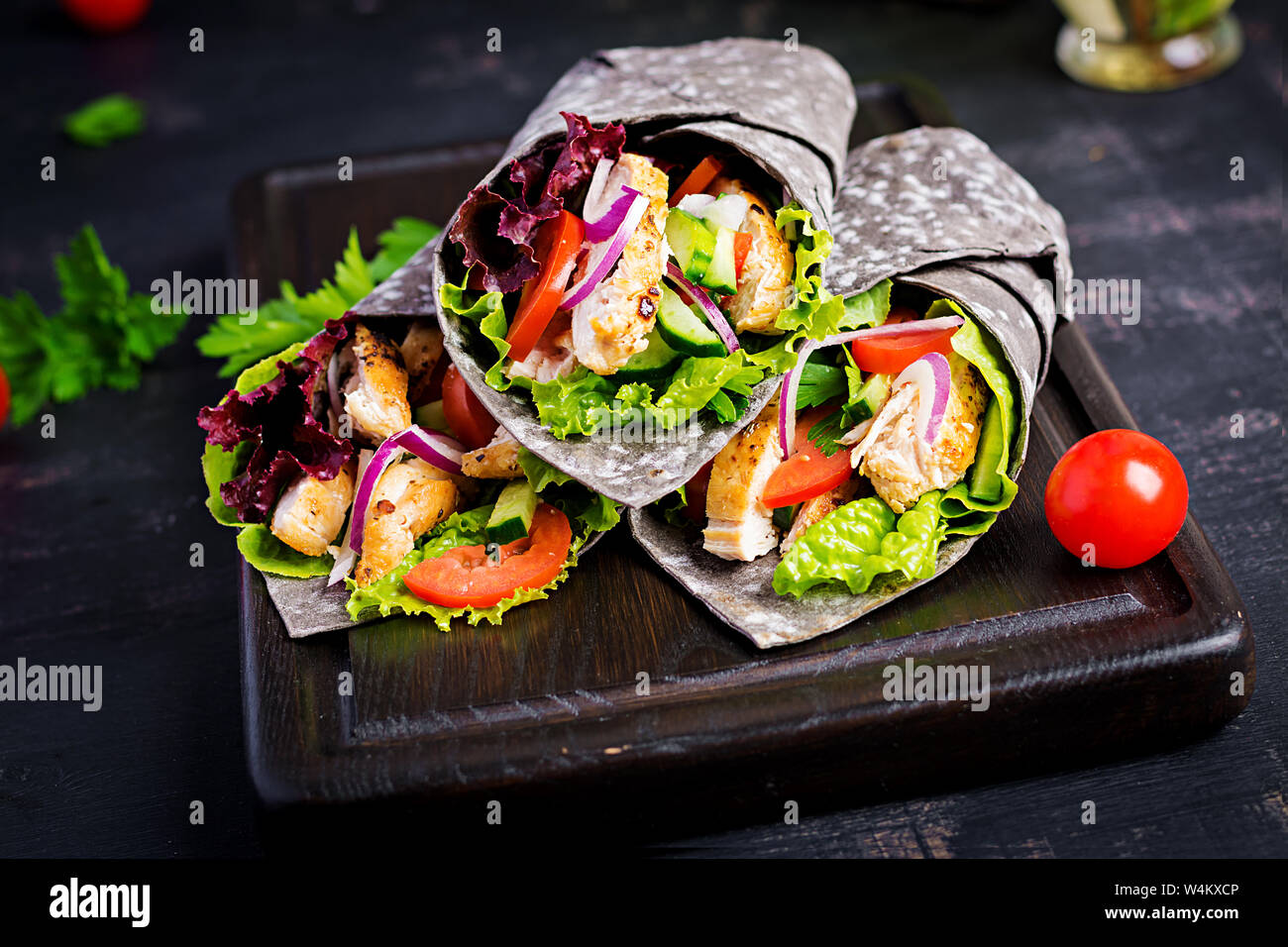 Tortilla mit Tinte Tintenfisch Wraps mit Hähnchen und Gemüse auf schwarzem Hintergrund. Chicken burrito, mexikanisches Essen. Stockfoto