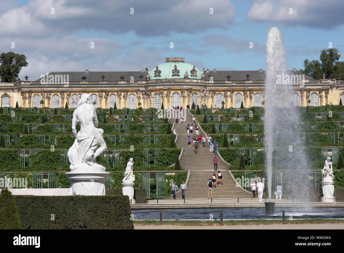 Menschen zu Fuß am Brunnen im Park von Sanssouci gegen Schloss Sanssouci, Potsdam, Deutschland. Der Park ist der Teil des UNESCO-Weltkulturerbe seit 1990 Stockfoto