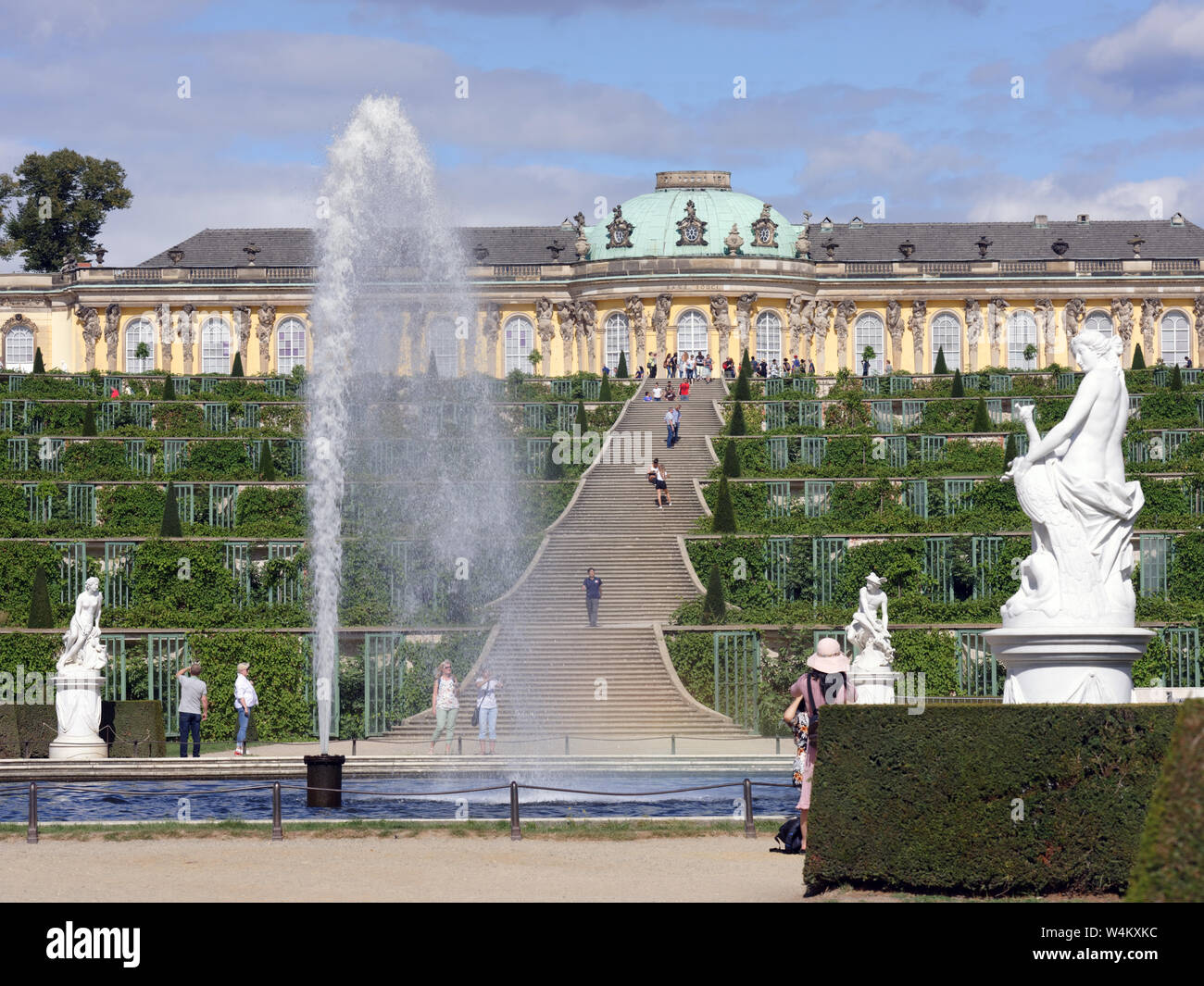 Menschen zu Fuß am Brunnen im Park von Sanssouci gegen Schloss Sanssouci, Potsdam, Deutschland. Der Park ist der Teil des UNESCO-Weltkulturerbe seit 1990 Stockfoto