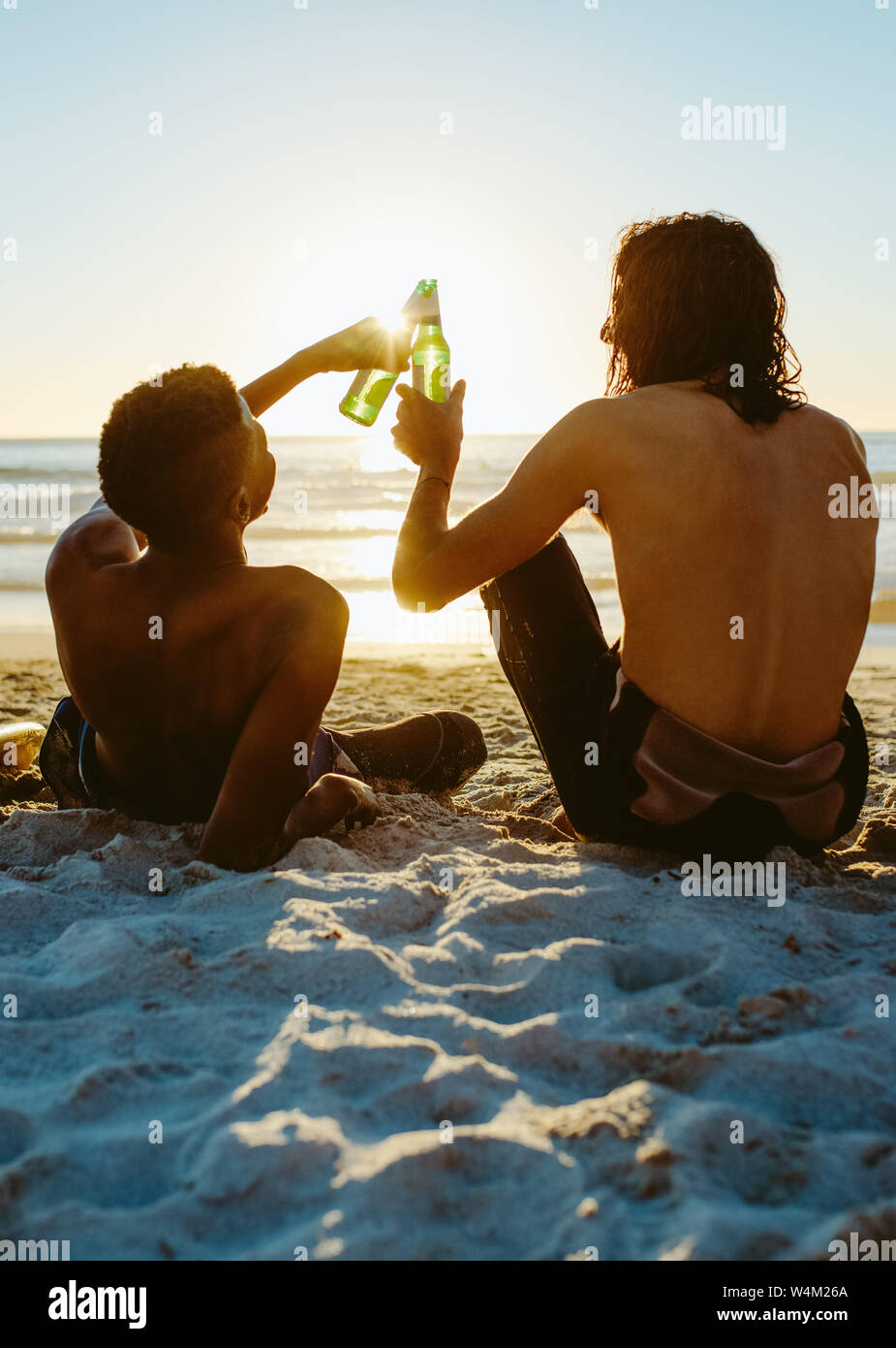 Ansicht der Rückseite zwei junge Freunde am Strand zu sitzen und toasten Bier beim Sonnenuntergang. Junge Leute feiern in der Strand mit Bier. Stockfoto