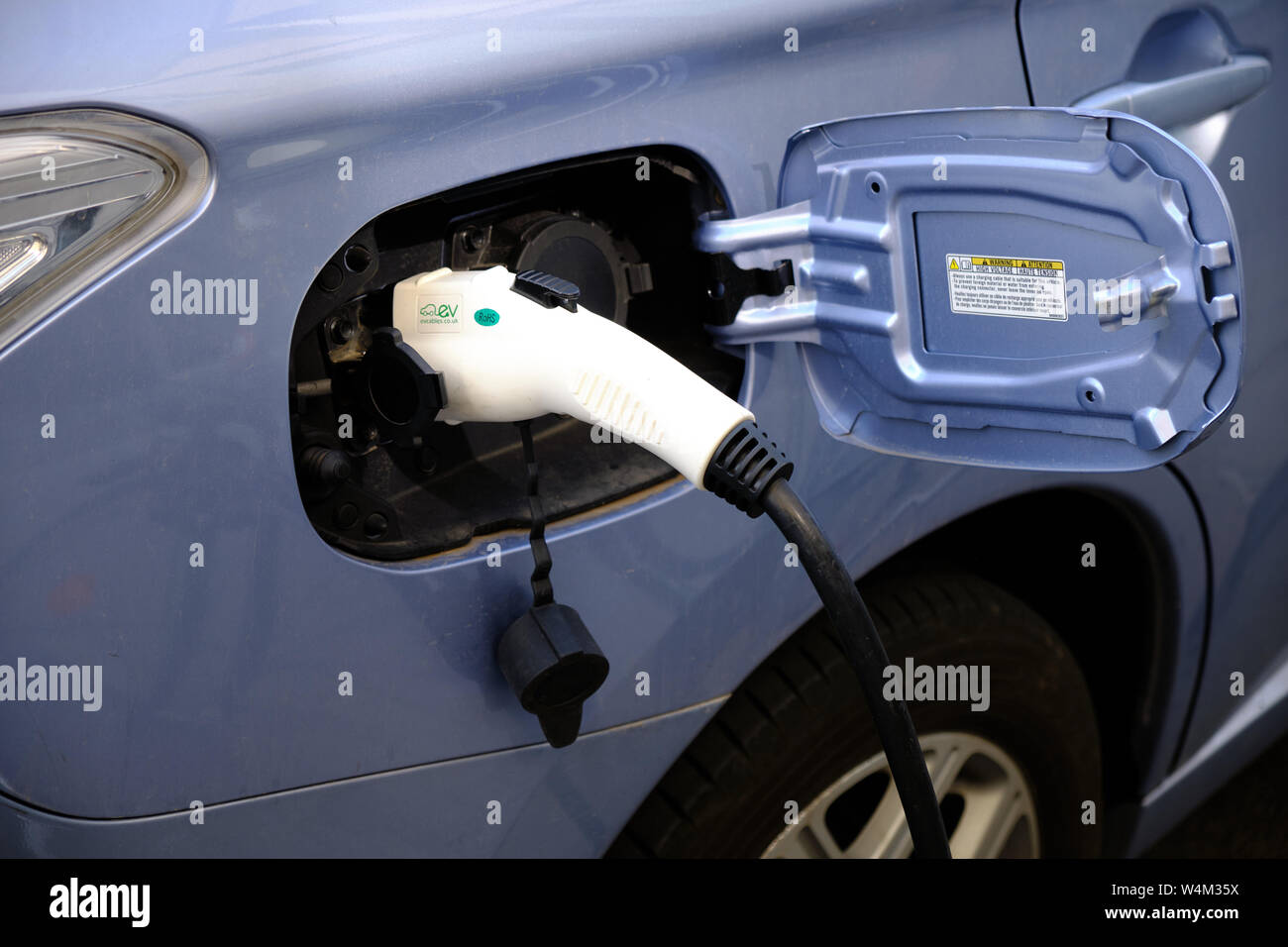 In der Nähe von EV-Elektroauto Ladestecker zu einem blauen Auto verbunden Stockfoto