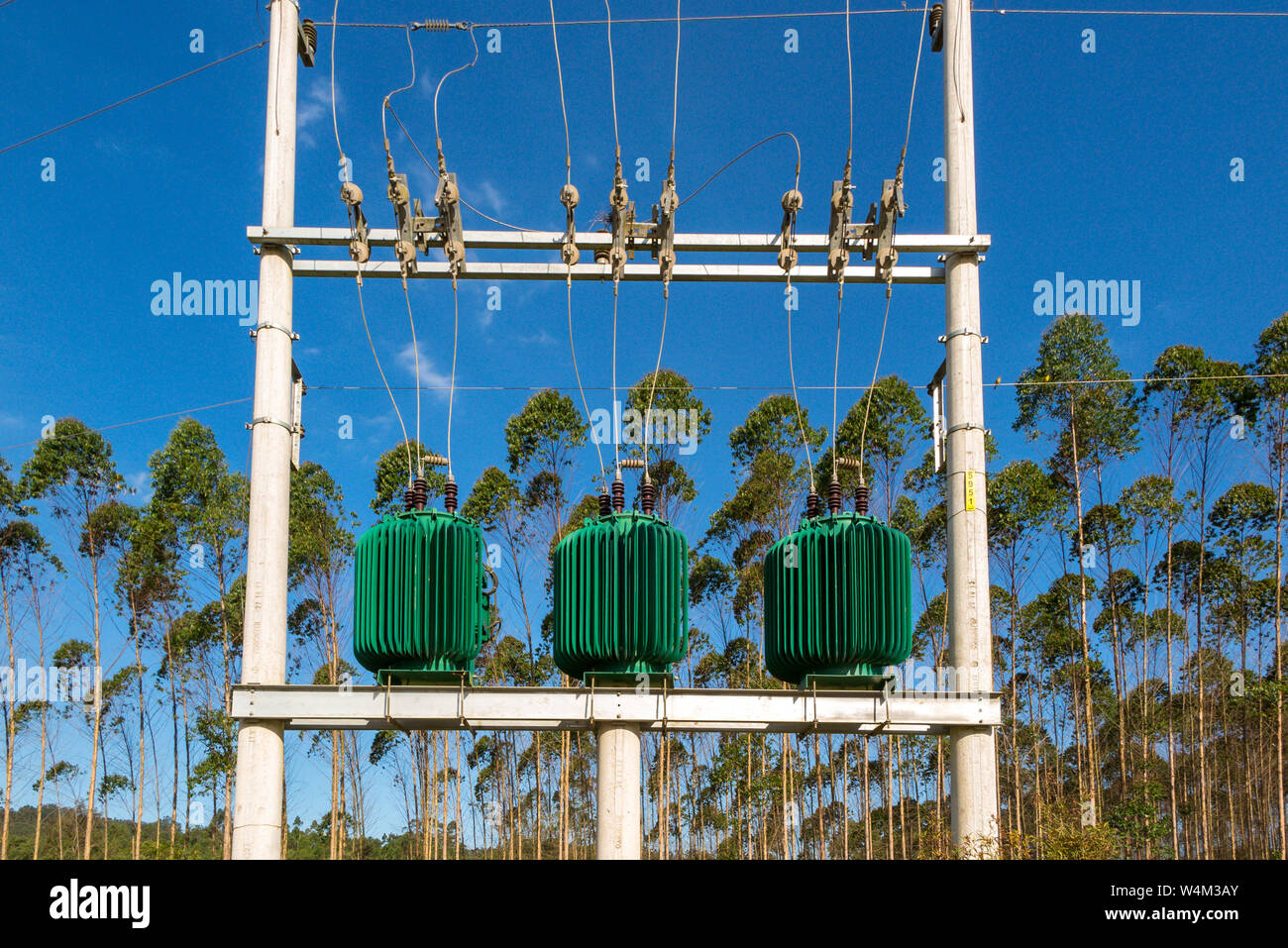 Drei grüne Energie Transformatoren in konkreten elektrische Struktur mit mehreren Drähten, Bäume und blauen Himmel im Hintergrund Stockfoto