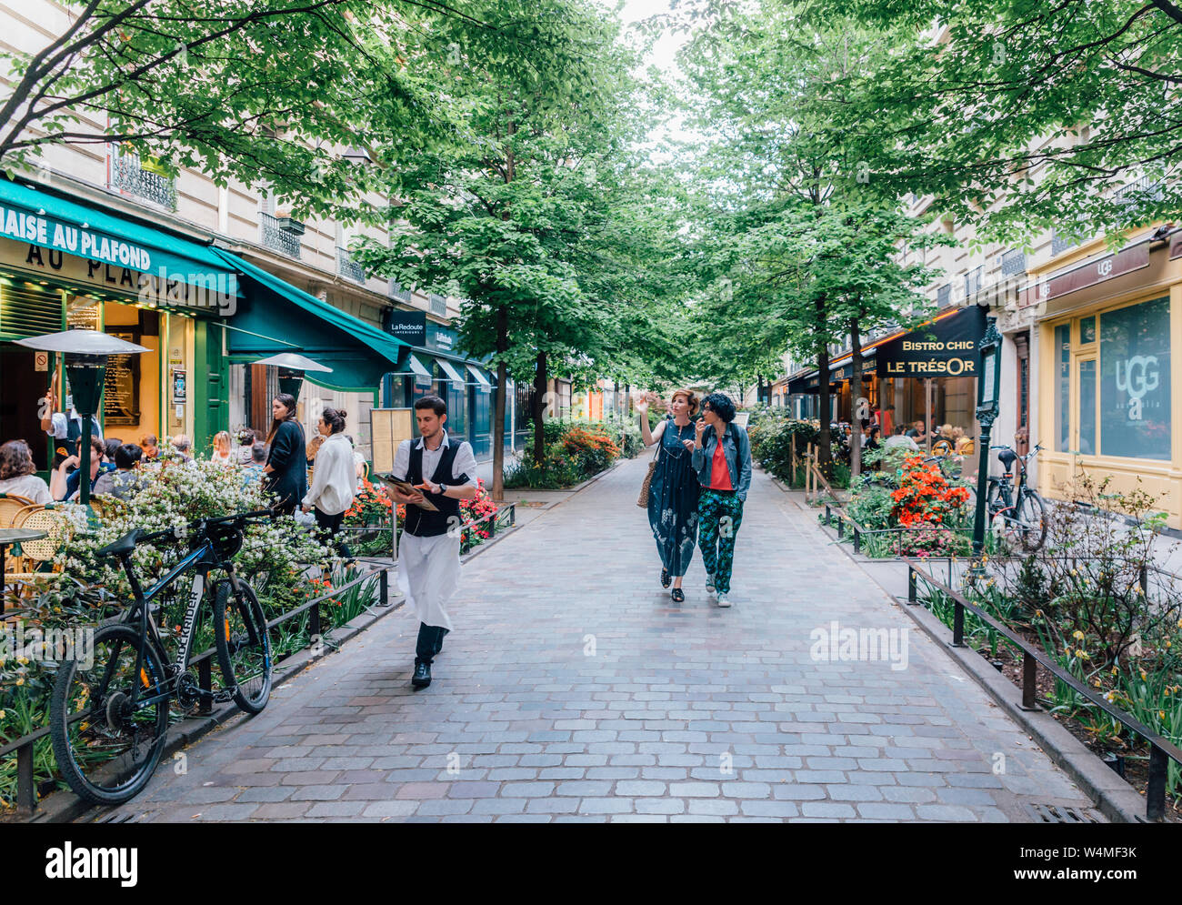 Paris, Frankreich - 8. Mai 2016: Leute, ein Café und ein Gespräch an einem ruhigen und charmanten Baum genießen gesäumten Straße im böhmischen Marais-Viertel von Paris. Stockfoto