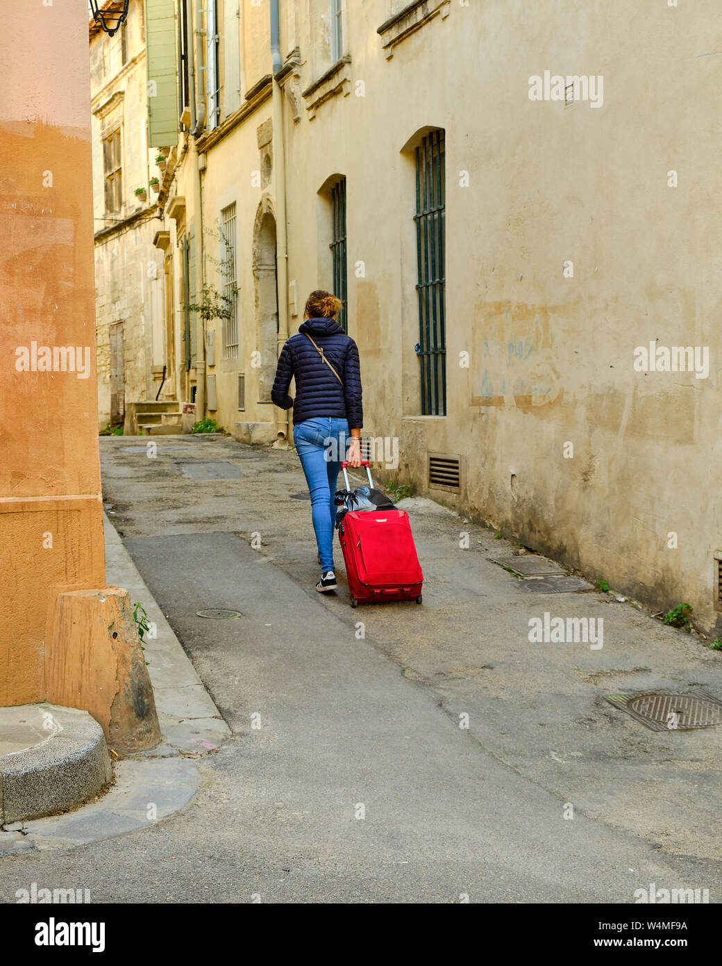 Junge Frau, Wandern, Ziehen einer roten rollenden Koffer die Gasse der Altstadt von Arles, Frankreich Stockfoto