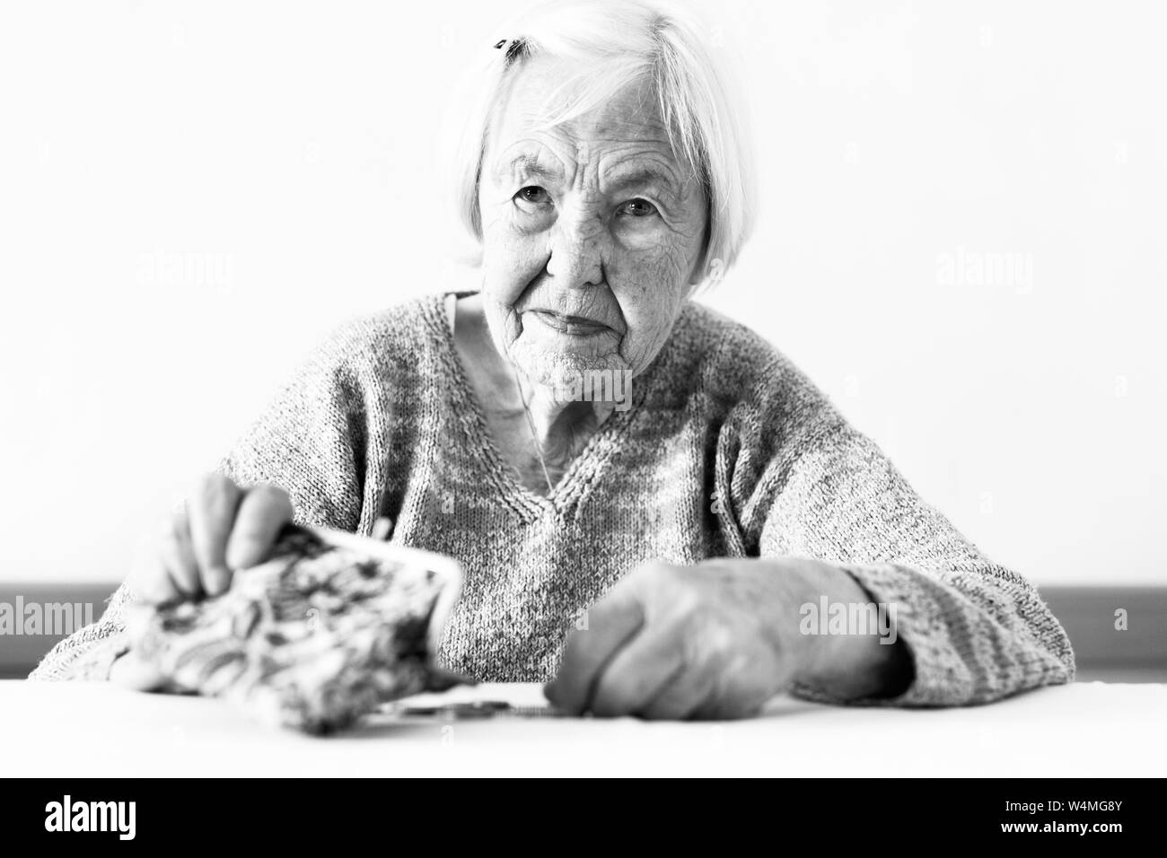 Betroffene ältere Frau am Tisch sitzen zählen Geld in Ihrem Portemonnaie. Schwarz-weiß Foto. Stockfoto