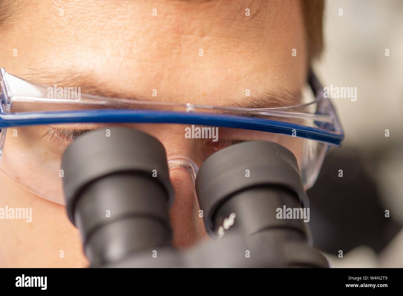 Nahaufnahme des Gesichts eines Forschers tragen Schutzbrille und schauen in die augenmuscheln eines Mikroskops in einem Biotechnologie Labor an der Johns Hopkins University in Baltimore, Maryland, 21. Januar 2010. Vom Homewood Sammlung Fotografie. () Stockfoto