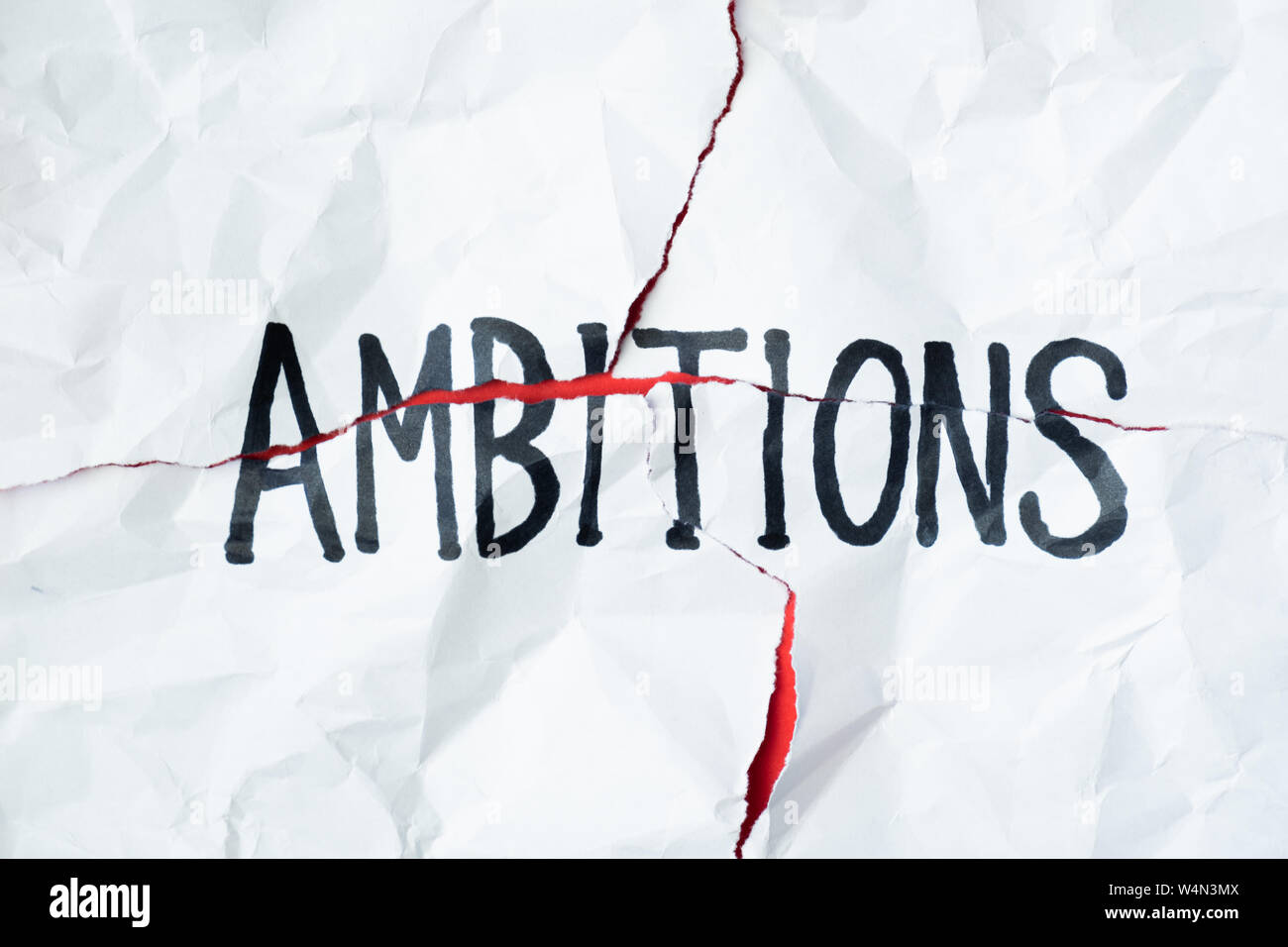 Wort "Ambitionen" handschriftlich auf zerknitterte zerrissenes Papier, Ansicht von oben. Zeichen, Konzept der gescheiterten Pläne und Hoffnungen, abstrakte anschauliches Bild Stockfoto