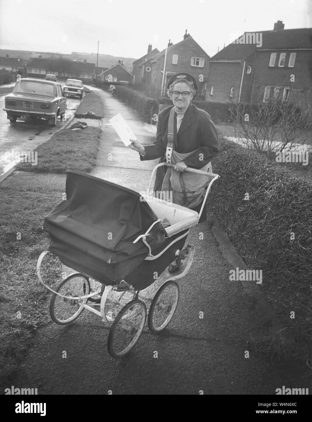 1980 s, historische, eine ältere postwoman mit einem traditionellen Coach -  Kinderwagen, gebaut auf einer Wohnsiedlung kämmen Ihre postalischen Auftrag  und Aufgaben einer Großmutter, England, UK Stockfotografie - Alamy