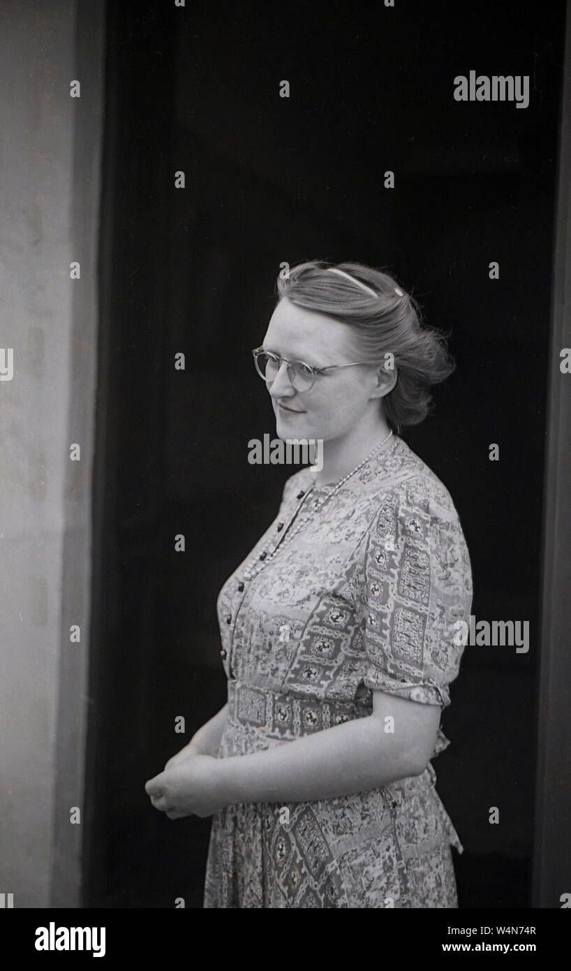 1950, historische, eine junge Engländerin mit gebunden Haar und trägt ein Kleid an einen Eingang, England, UK. Stockfoto