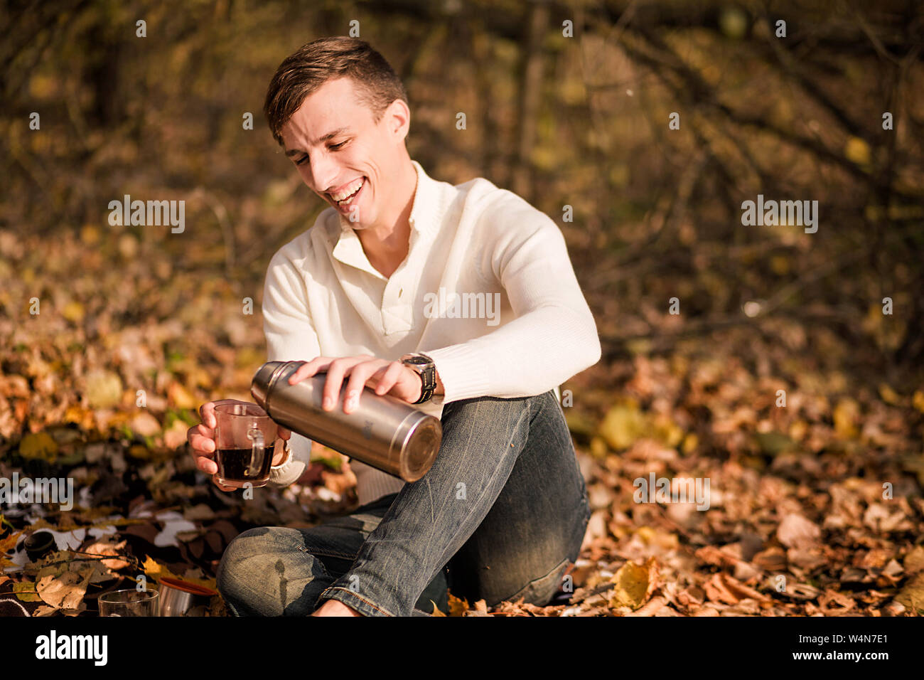 Foto eines Mannes gießt Tee aus einer Thermoskanne in eine Tasse in den Wald Stockfoto