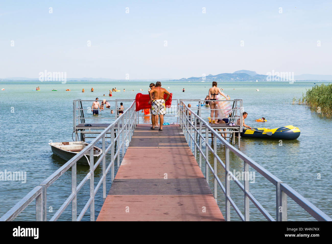 Die badegäste entlang Pier in Plattensee, Ungarn zu baden. Die Berge und die Burg Szigliget im Hintergrund. Stockfoto