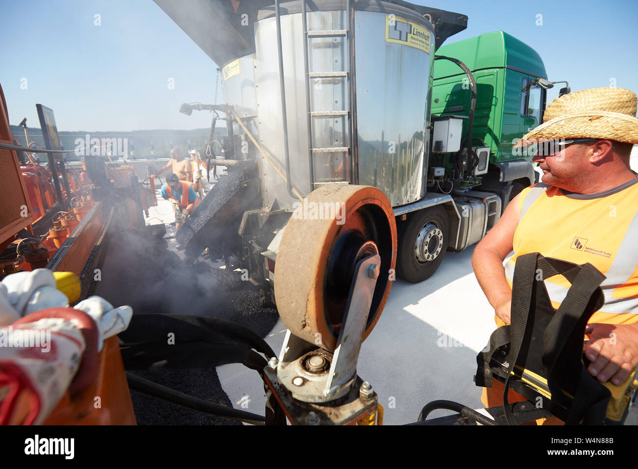 Zeltingen Rachtig, Deutschland. 24. Juli, 2019. Arbeitnehmer, die Asphaltierung der Straße Oberfläche des Hochmosel Brücke im Bau bei Temperaturen weit über 30 Grad Celsius. Es gibt keine schattigen Platz auf dem 160 Meter hohen Gebäude über dem Moseltal. Quelle: Thomas Frey/dpa/Alamy leben Nachrichten Stockfoto