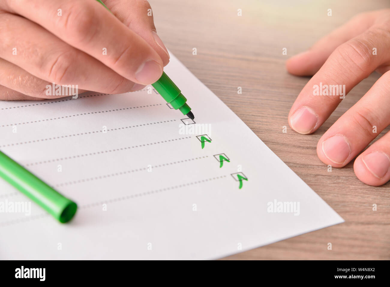 Konzept der Hand mit grünen Marker Pen das Ausfüllen eines Fragebogens auf ein Blatt Papier auf einem Holztisch. Horizontale Komposition. Erhöhte anzeigen. Stockfoto