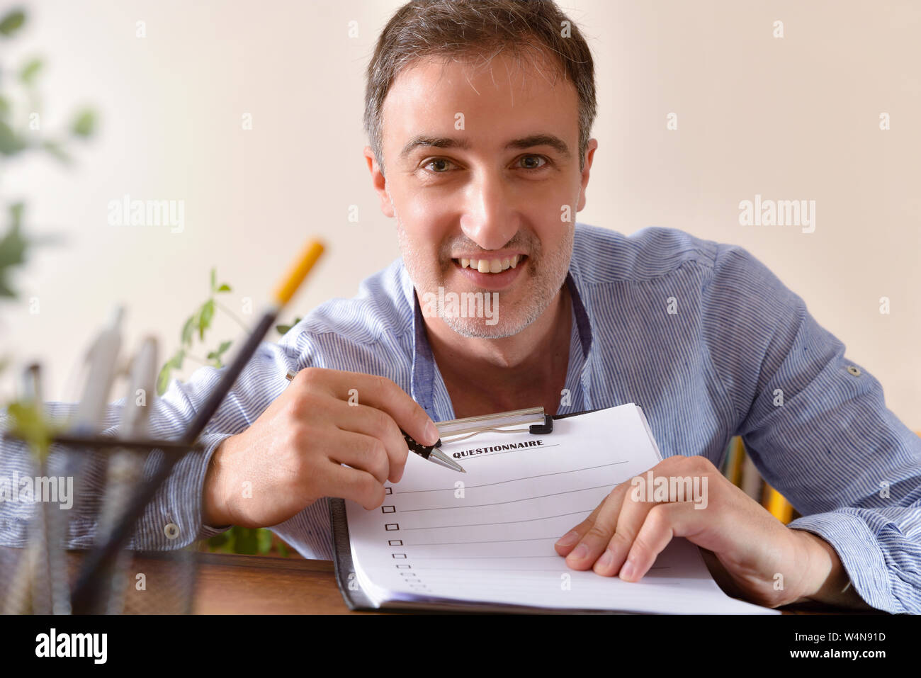 Mann in blau gestreiften Shirt, das einen Fragebogen auf einem hölzernen Tisch in einem Zimmer. Horizontale Komposition. Vorderansicht. Stockfoto