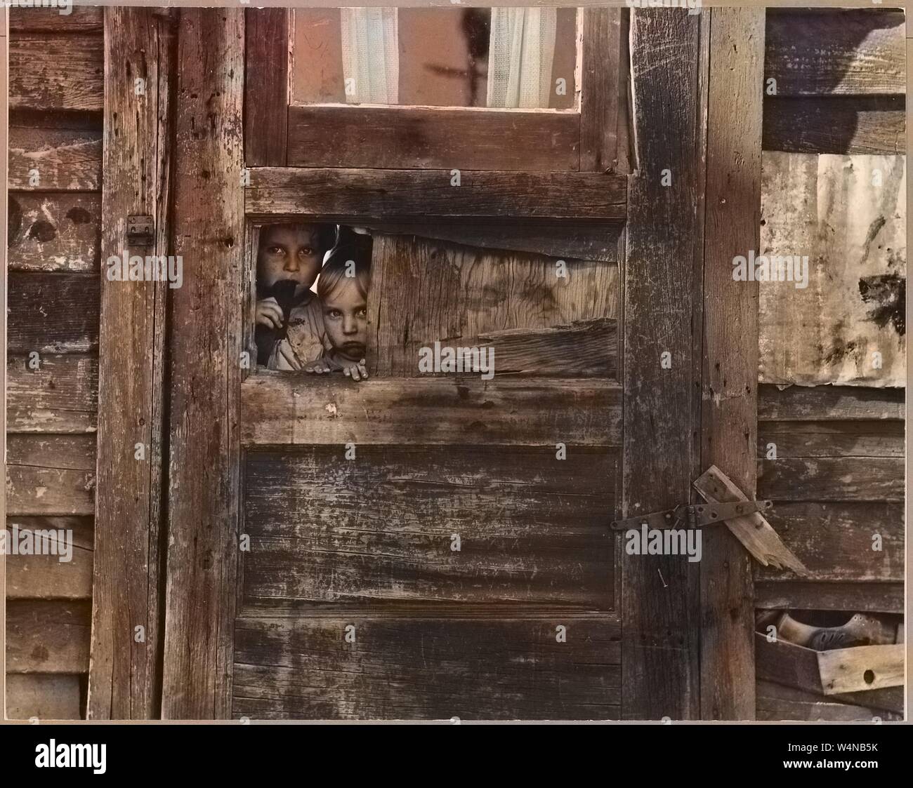 Kinder von Wanderarbeitnehmern spähen durch ein Loch in der ihr Lager Haus in Kern County, Kalifornien, 1940. Hinweis: Das Bild hat digital über ein modernes Prozess eingefärbt worden. Farben möglicherweise nicht sein - genau. Mit freundlicher Genehmigung der nationalen Archive. () Stockfoto