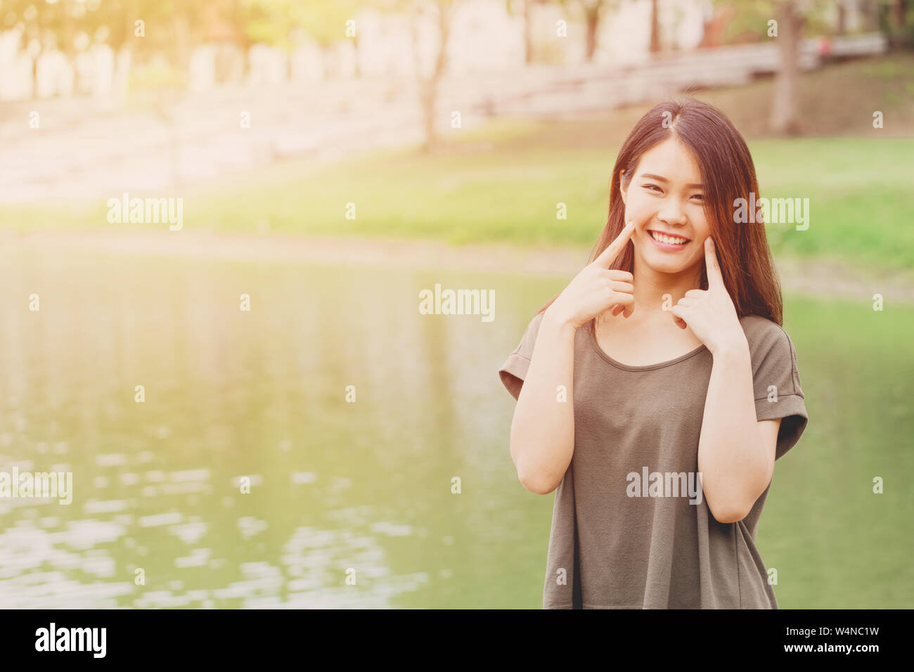 Süße asiatische Mädchen Hand an der Wange lächelnd an Wasser See Park im Freien sonnigen Tag Stockfoto