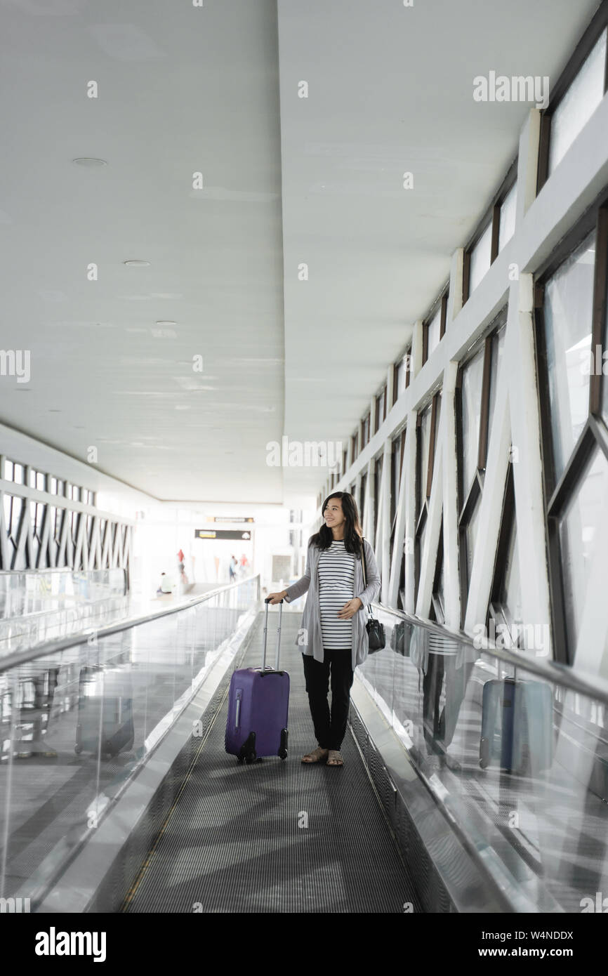 Asiatische schwangere Frauen ziehen Koffer, während die Rolltreppe vorbei gehen. Stockfoto Asiatische schwangere Frauen ziehen Koffer, während die Rolltreppe vorbei gehen. Stockfoto