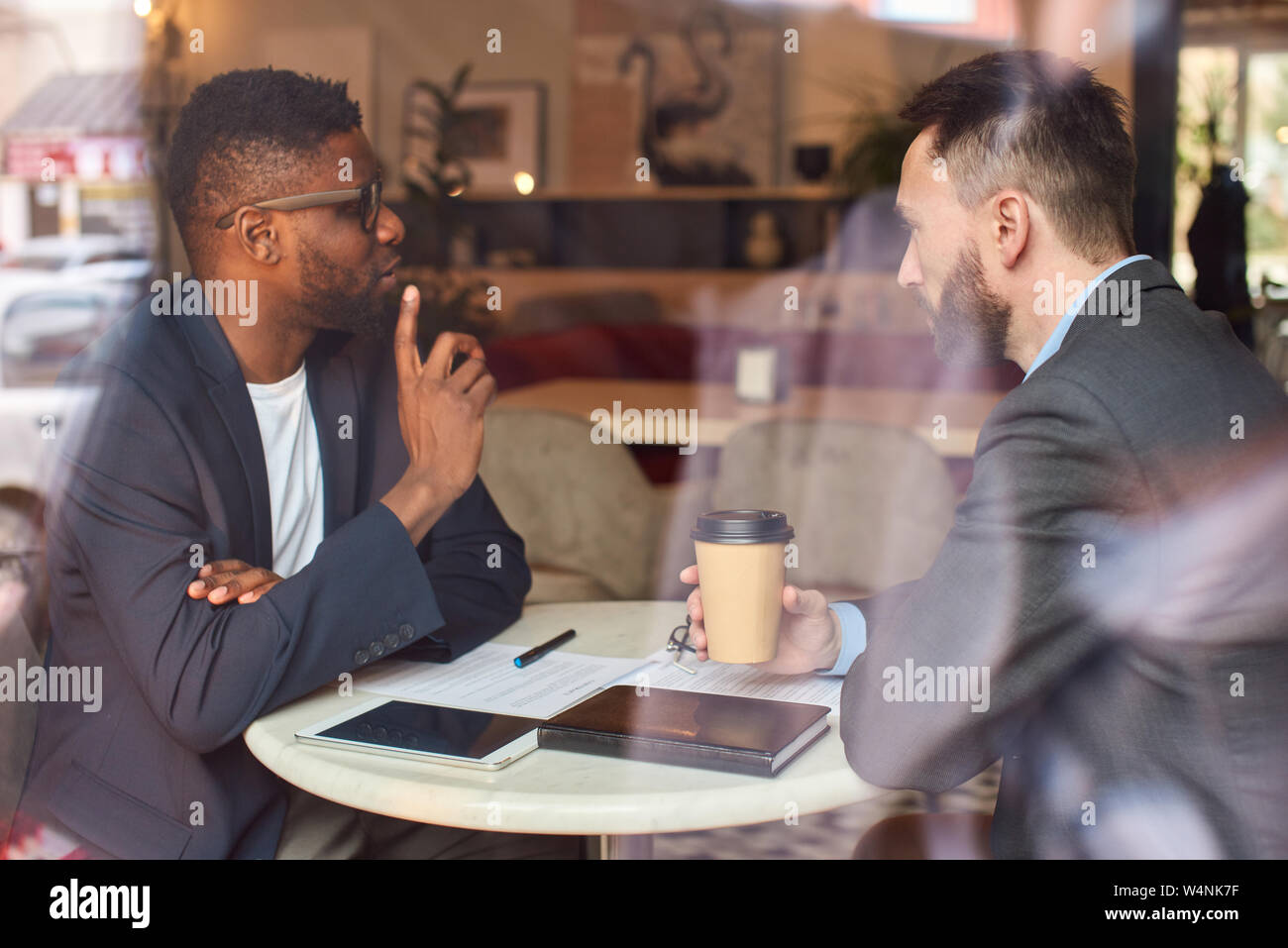 Zwei Männer in Anzügen sitzen im Cafe, trinken Kaffee und haben geschäftliche Gespräche, während sie durch den Dokumenten suchen. Stockfoto