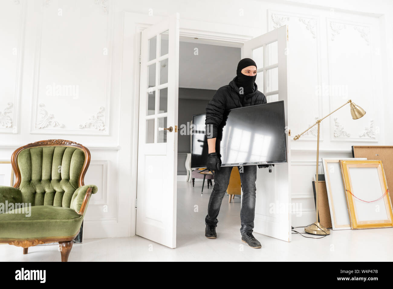 Dieb mit schwarzer Sturmhaube stehlen Moderne teure Fernseher. Luxus Apartment mit Stuck. Man Einbrecher stehlen tv aus dem Haus Stockfoto
