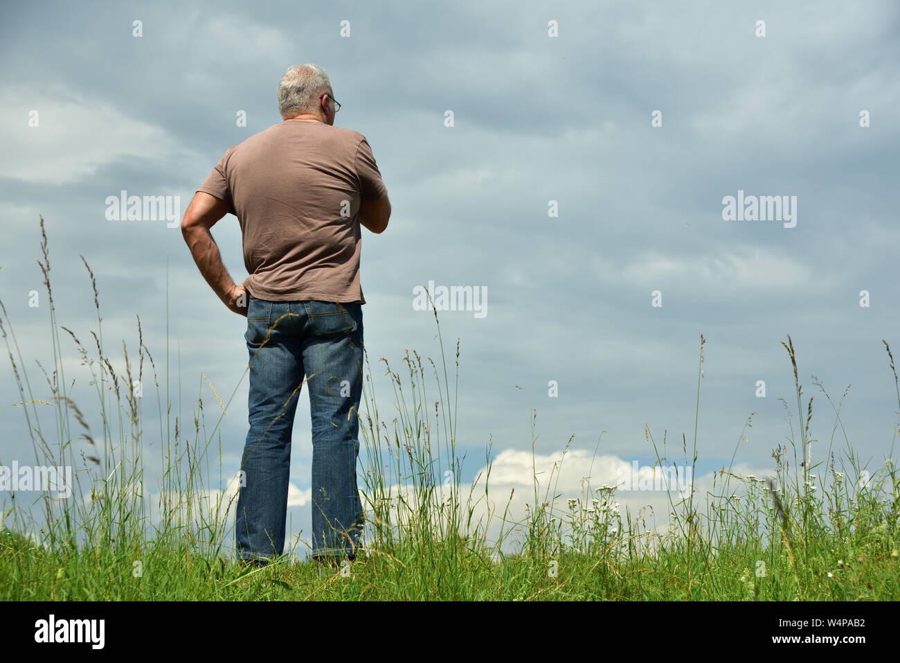 Ein Mann steht auf einer Wiese gegen einen bewölkten Himmel und schaut in die Wolken Stockfoto