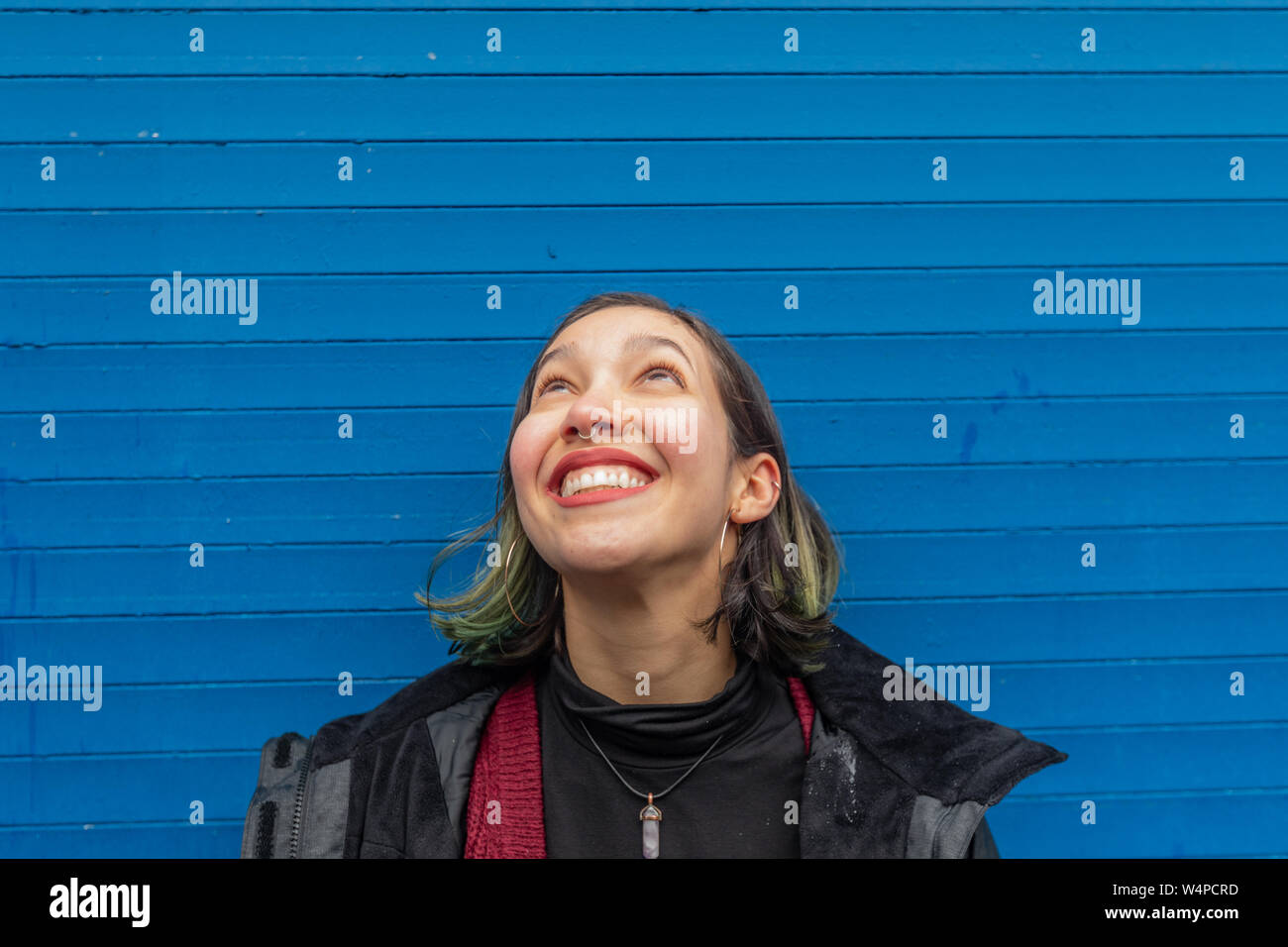 Lächelnde Frau sucht auf der Regen auf ihrem Gesicht, auf der blauen Wand. Stockfoto