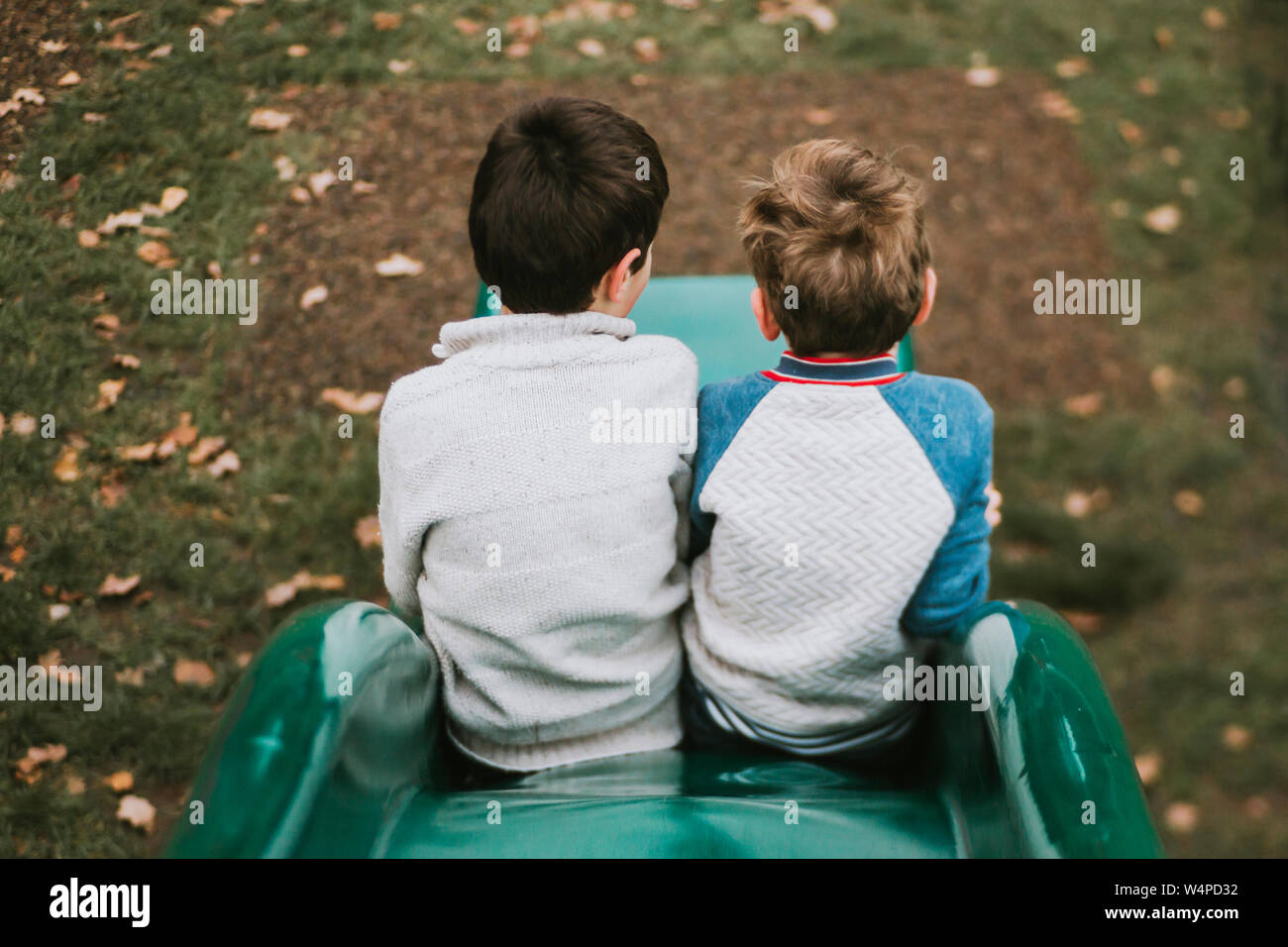 Ansicht der Rückseite zwei Brüder sitzen auf Folie am Spielplatz Stockfoto