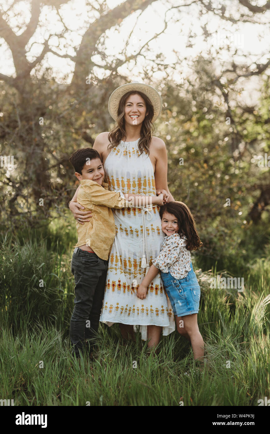 Porträt der Mutter umarmt Sohn und Tochter im Feld mit Hintergrundbeleuchtung Stockfoto