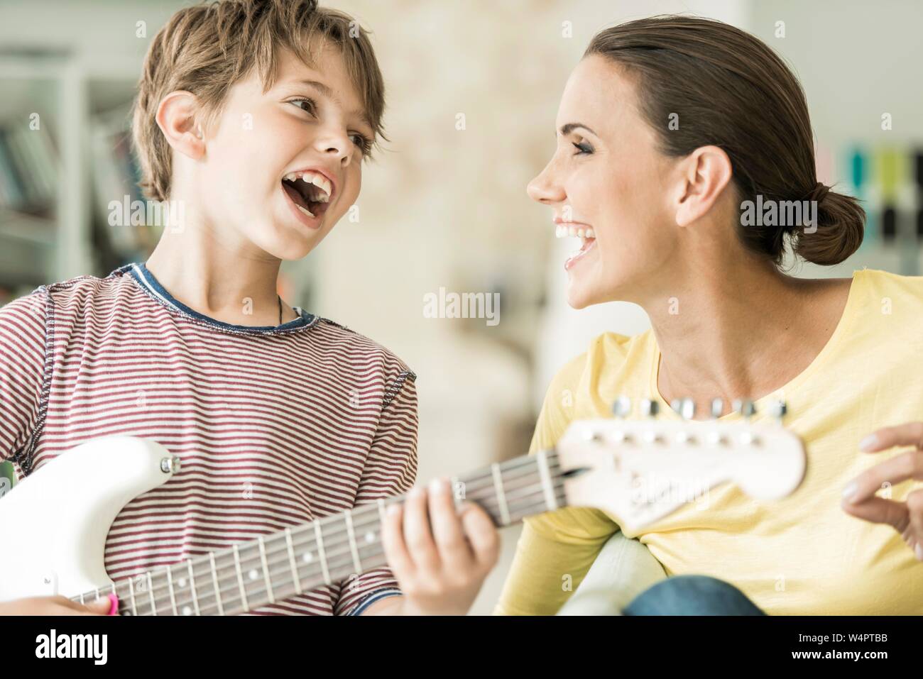Mutter und Sohn gemeinsam Musik machen, beide singen und Sohn spielen, E-Gitarre, close-up, Lachen, Deutschland Stockfoto