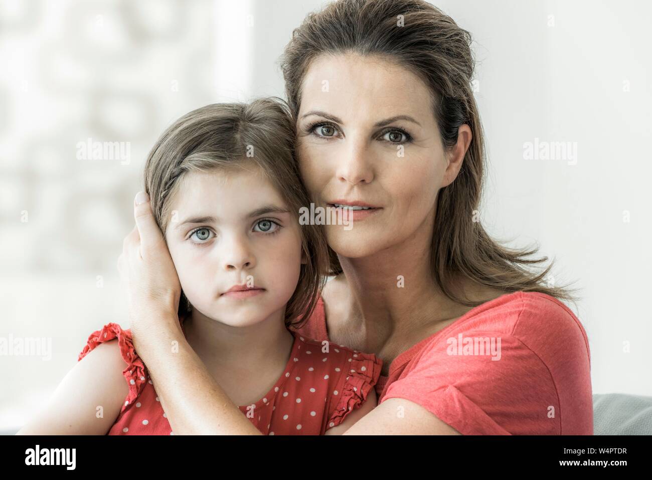 Mutter und Tochter sitzen zusammen auf der Couch und in die Kamera schauen, Mutter hält schützende Hand um Tochter, Deutschland Stockfoto
