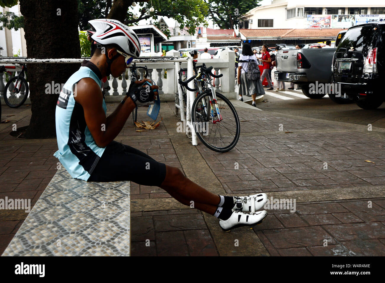ANTIPOLO CITY, Philippinen - Juli 23, 2019: ein Biker ruht und sitzt auf einer Parkbank, während sie sein Smartphone. Stockfoto