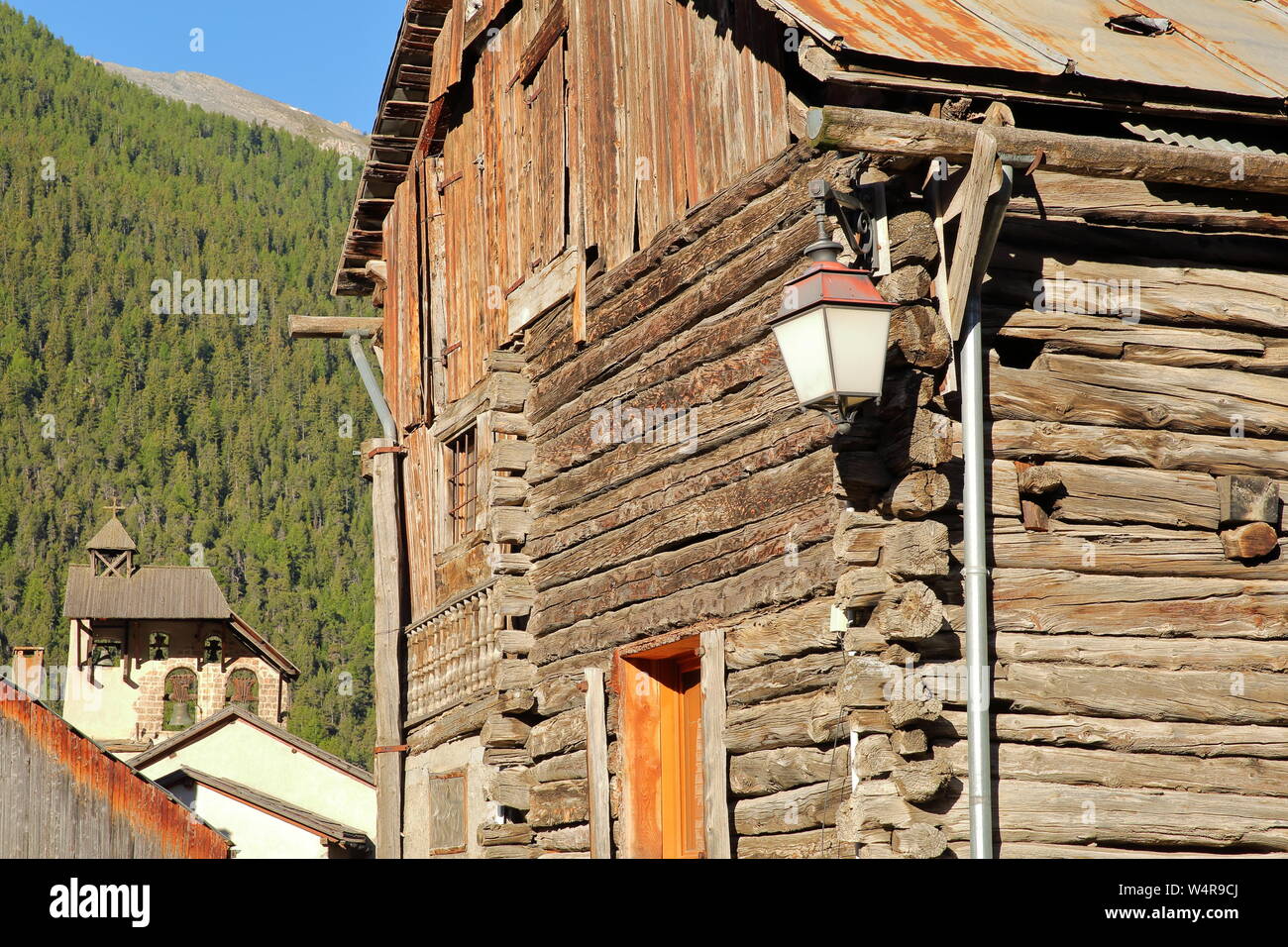Traditionellen Holzhaus mit dem Glockenturm von Saint Sebastien Kirche im Hintergrund, Ceillac, Naturpark Queyras, Südliche Alpen, Frankreich Stockfoto