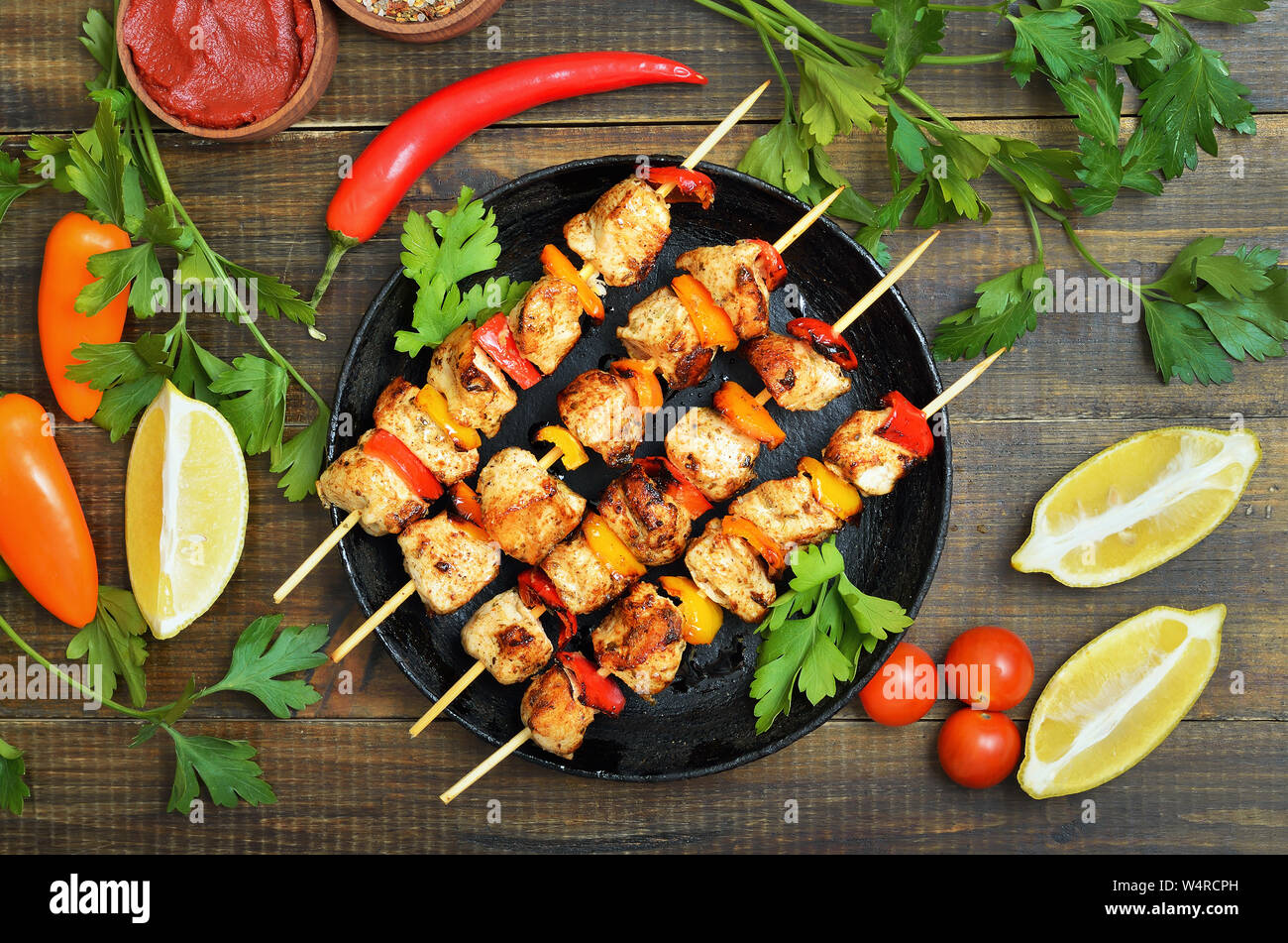 Gegrilltes Hühnchen Kebab mit Paprika in der Pfanne, Gemüse und Kräutern auf Holztisch, Ansicht von oben Stockfoto