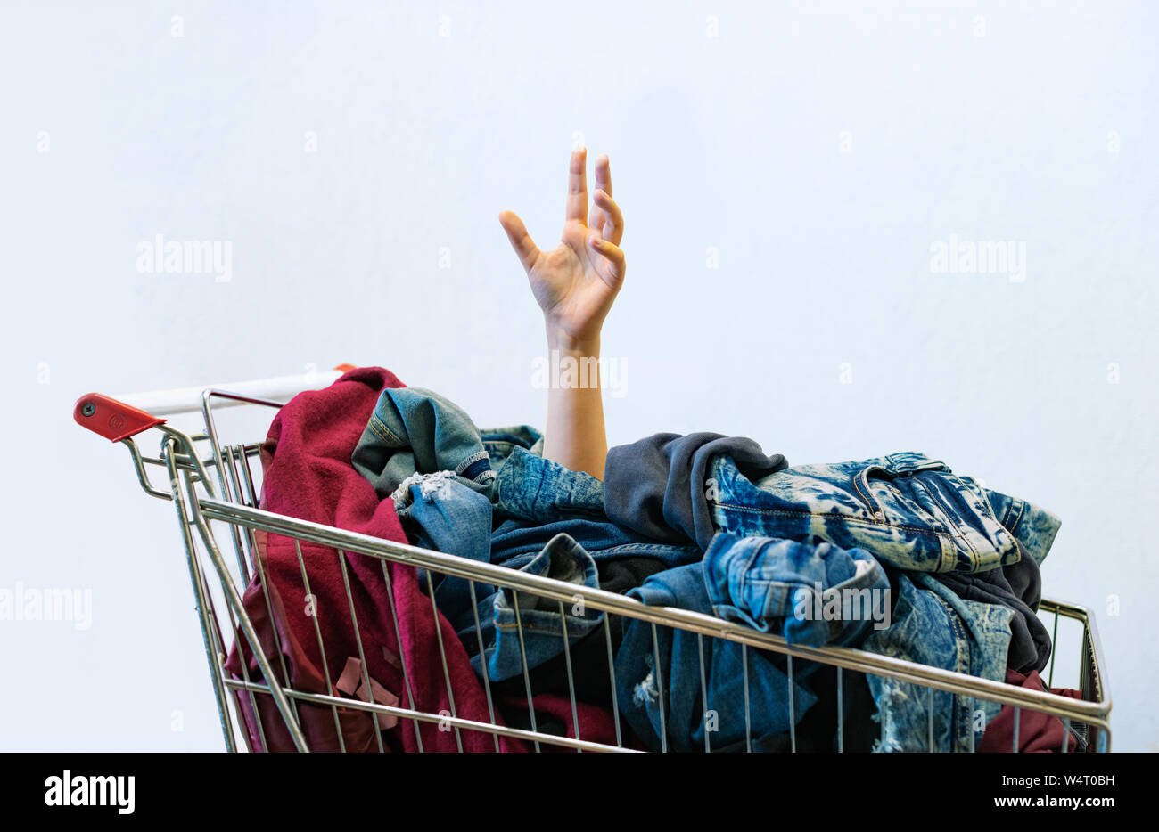 Shopaholic Konzept. Weibliche Hand ragt aus dem Warenkorb voller Kleider. Unkontrollierbare Shopping - ZWANGHAFTE STÖRUNG oder oniomania kaufen. Co Stockfoto