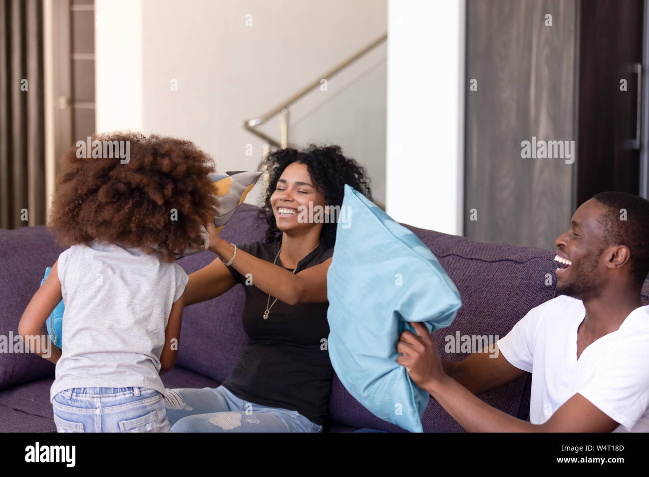 Fröhliche afrikanischen Familie und niedliche kleine Tochter kämpfen mit Kissen Stockfoto