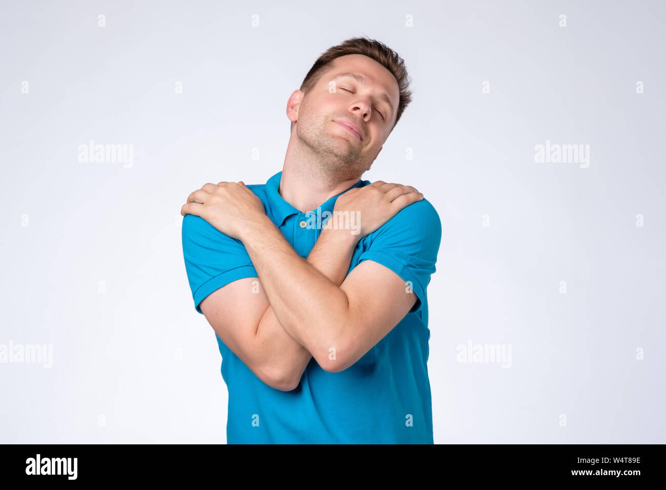Mann breit grinsend, umarmt sich und fühlt sich geschützt. Stockfoto