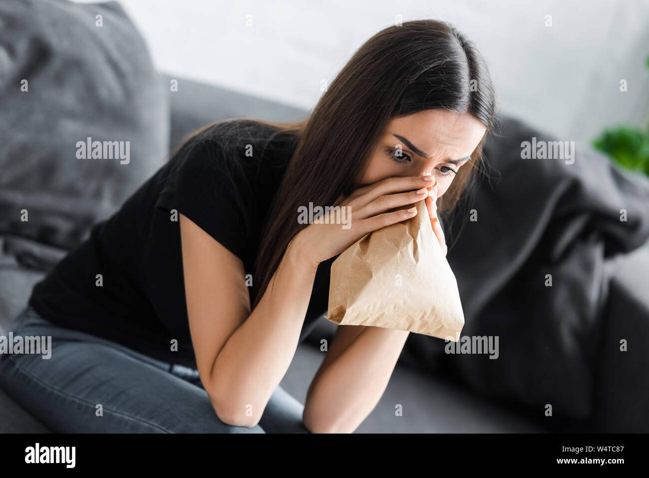 Junge Frau die Atmung in Papiertüte während leidet unter Panikattacken zu Hause Stockfoto