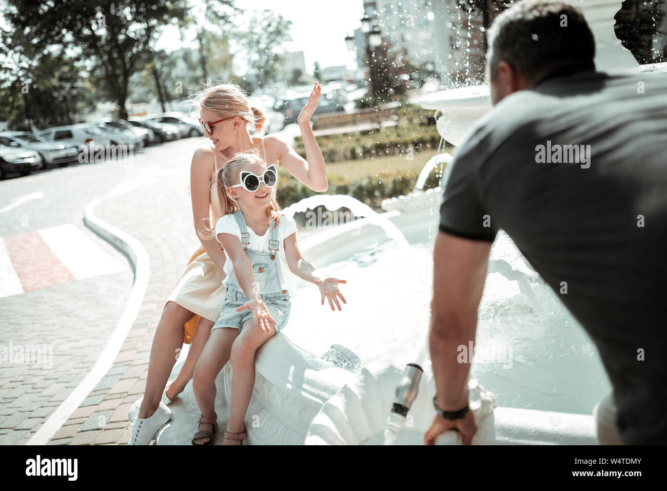 Beste Familie. Fröhliches kleines Mädchen spielen mit ihren Eltern in der Nähe von wunderschönen weißen Brunnen in der Stadt. Stockfoto