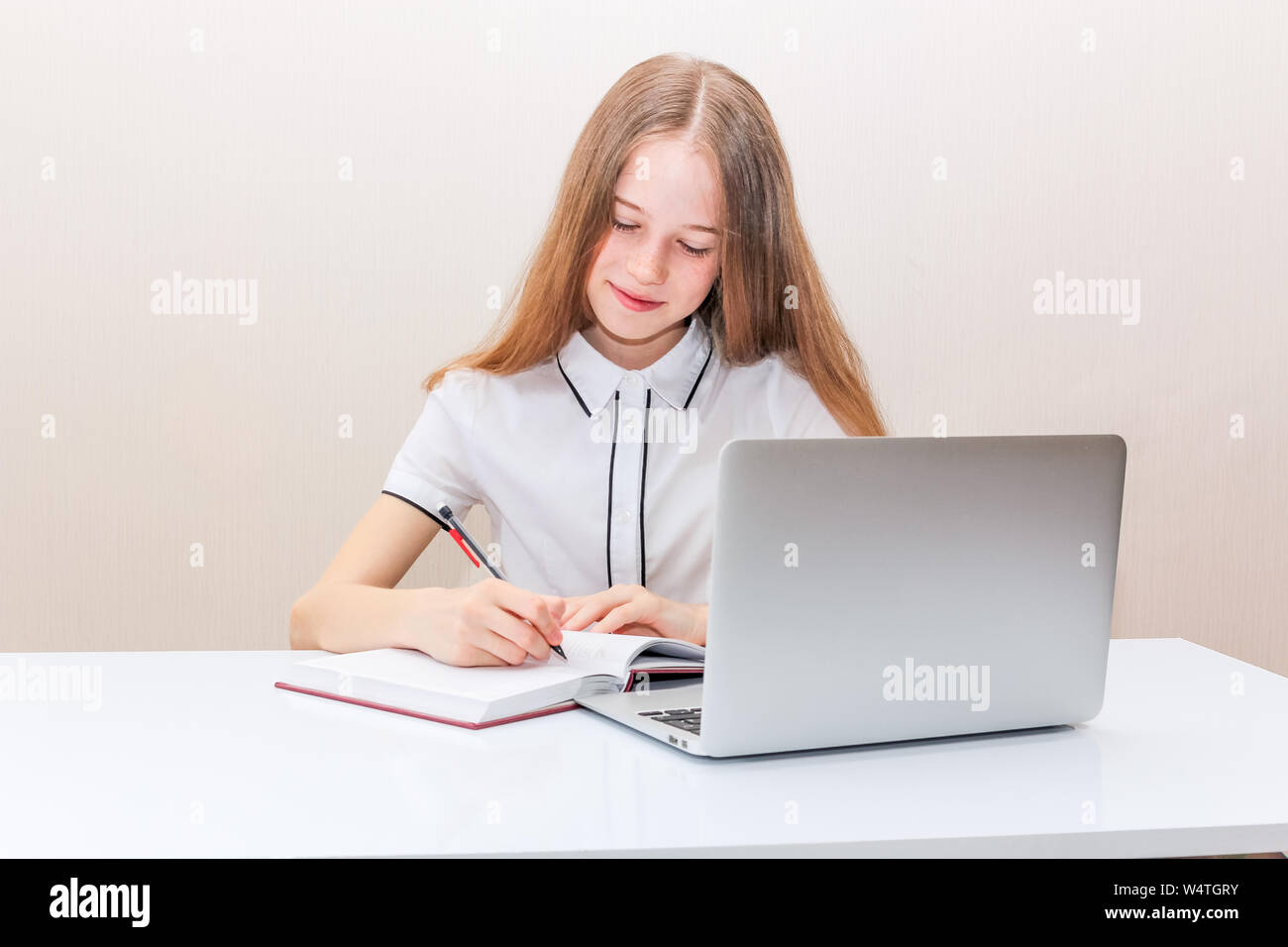 Junges Mädchen mit blonden Haaren in einer weißen Bluse sitzt am Tisch und schaut in den Laptop monitor Stockfoto