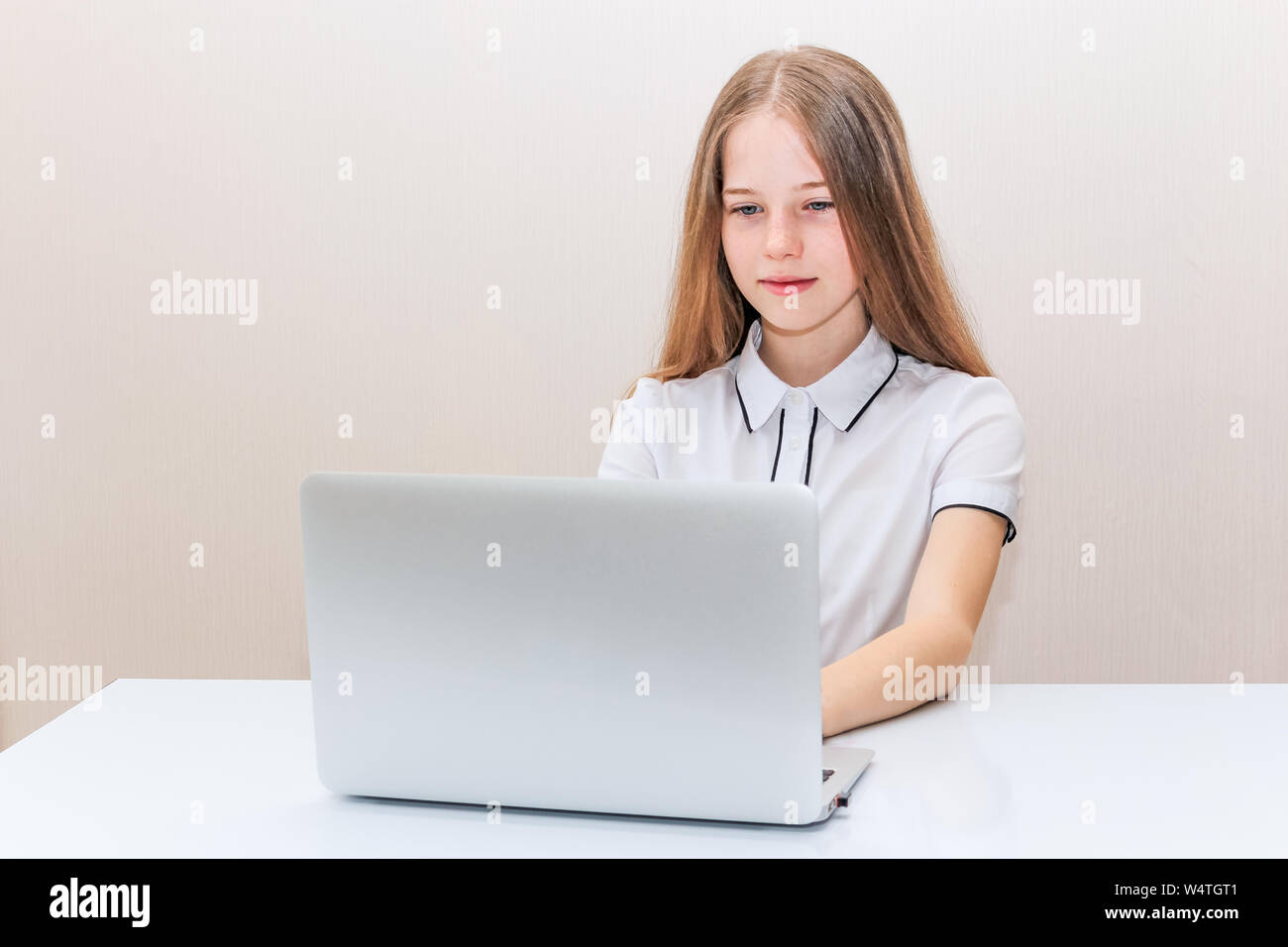 Junges Mädchen mit blonden Haaren in einer weißen Bluse sitzt am Tisch und schaut in den Laptop monitor Stockfoto