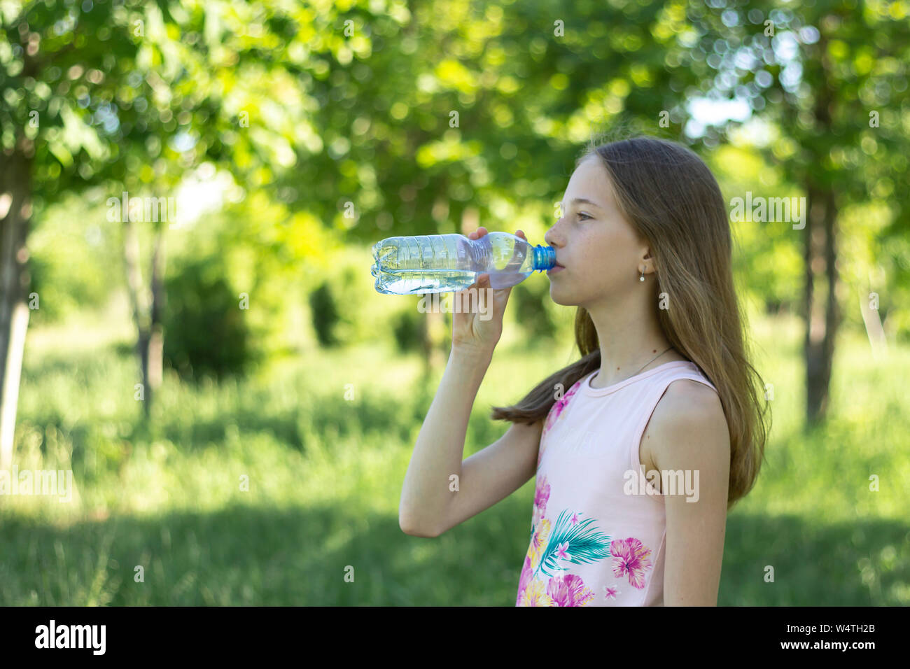 Ein junges blondes Mädchen in einem rosa T-Shirt Getränke Wasser aus der Plastikflasche auf einem Hintergrund von grünen Wald Stockfoto