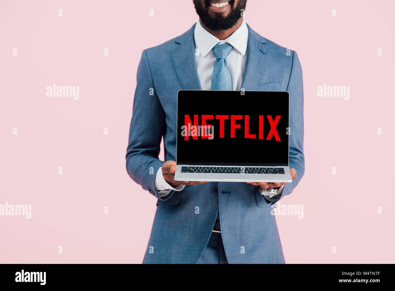 Kiew, Ukraine - Mai 17, 2019: 7/8 Ansicht der lächelnden afrikanischen amerikanischen Geschäftsmann, Laptop mit Netflix website, isoliert auf Rosa Stockfoto