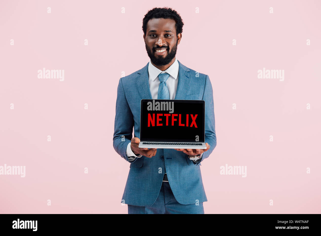 Kiew, Ukraine - Mai 17, 2019: Lächelnde afrikanischen amerikanischen Geschäftsmann, Laptop mit Netflix website, isoliert auf Rosa Stockfoto