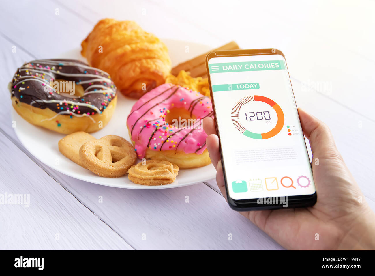 Kalorien zählen und die Lebensmittelüberwachung Konzept. Frau mit Kalorienzähler Anwendung auf Ihrem Smartphone mit Krapfen, Snack und Cookies auf der Platte an der Bac Stockfoto