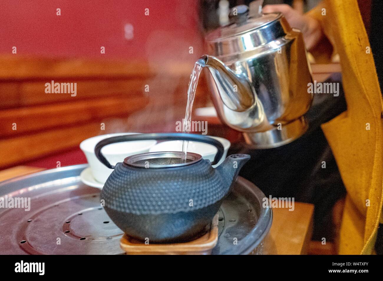Hand einer Frau gießen kochendes Wasser in eine gusseiserne Teekanne beim Durchführen einer Tee Zeremonie im Imperial Kaffee Gericht in der Gourmet Ghetto Nachbarschaft von Berkeley, Kalifornien, November 29, 2018. () Stockfoto